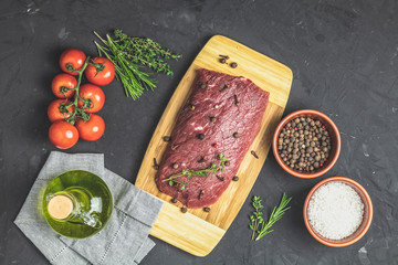 Beef steak on wooden cutting board with ingredients for cooking spices