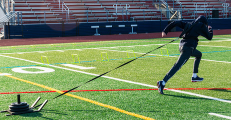 Athlete pulling sled with weights on turf field in cold weather - Powered by Adobe