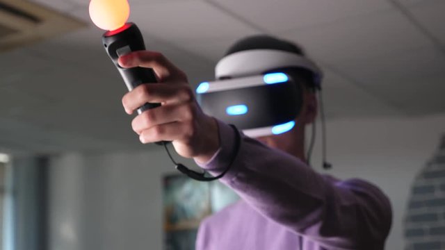 A gamer playing video game in virtual reality headset and using playstation. Portrait of young man playing VR.