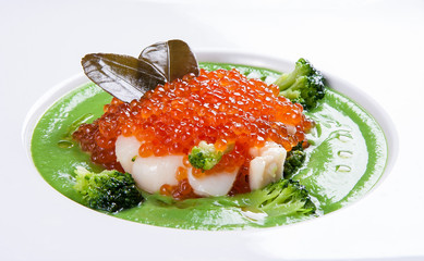 Cream of broccoli soup with scallops and red caviar, on white background