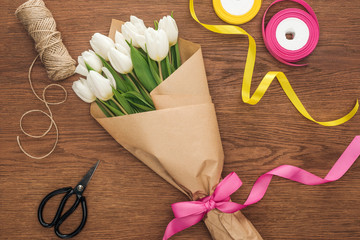 top view of spring tulip bouquet with ribbons and craft paper on wooden background