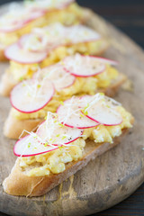 Scrambled eggs, radish and micro greens toasts seasoned with ground pepper. Wooden board, high resolution