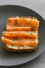 Rye sourdough toasts with butter, smoked salmon and dill. Grey ceramic plate, high resolution