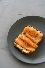 Rye sourdough toasts with butter, smoked salmon and dill. Grey ceramic plate, high resolution