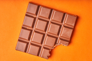 Bitten bar of milk chocolate on a colored paper background