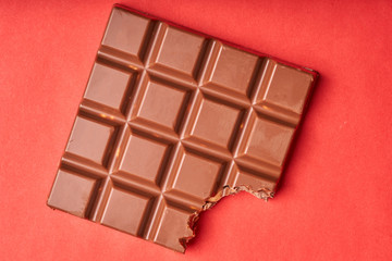 Bitten bar of milk chocolate on a colored paper background