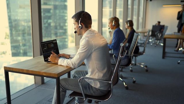 Back view of businesspeople in headsets using laptops while working in office