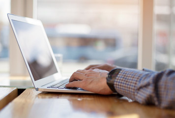 Cropped image of a young man working on his laptop in a coffee shop, rear view of business man hands busy using laptop at office desk, young male student typing on computer sitting at wooden table