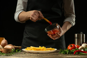 Chef with sauce and french fries ready, on the background with vegetables. Cooking tasty but harmful food. Background for design and menu, home-made recipe, cookbook. Fast food