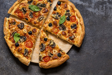 pizza with tomatoes, cheese, mushrooms, olives and spinach on a dark background