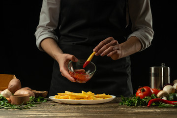 Chef with sauce and french fries ready, on the background with vegetables. Cooking tasty but harmful food. Background for design and menu, home-made recipe, cookbook. Fast food
