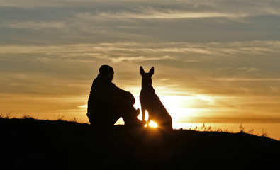 A man and a dog on the background of a beautiful sunset