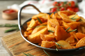 Metal dish with baked potatoes and rosemary on wooden board, closeup
