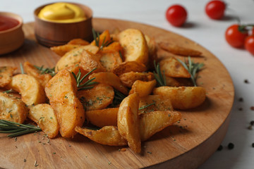 Wooden board with baked potatoes and rosemary on table, closeup