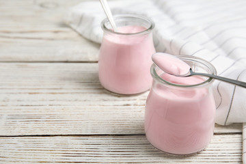 Glass jars with creamy yogurt served on white wooden table. Space for text