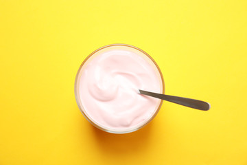 Fototapeta na wymiar Glass bowl with creamy yogurt and spoon on color background, top view