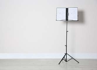 Note stand with music sheets near white wall indoors. Space for text - obrazy, fototapety, plakaty