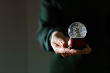 Woman holding Christmas snow globe on blurred background, closeup. Space for text