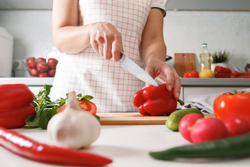 Obraz na płótnie Canvas Homemade cooking. A woman in the kitchen cuts red bell pepper on a cutting wooden board. Healthy fresh food