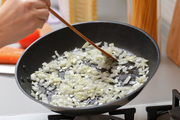 Homemade cooking. Woman fry onions in a hot pan with vegetable oil. Close-up.