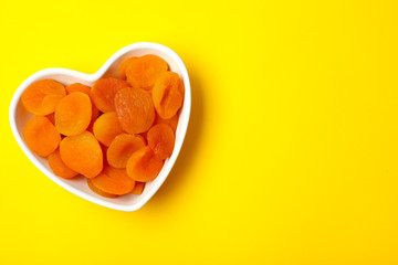 Bowl of dried apricots on color background, top view with space for text. Healthy fruit