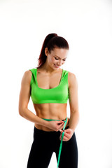 Attractive female bodybuilder measuring her waist with measurement tape. Photo of young woman in sportswear on white background.