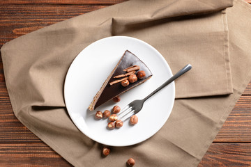 Plate with piece of tasty chocolate cake with hazelnuts on table