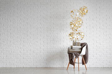 Chair with gifts and balloons near white brick wall © Pixel-Shot