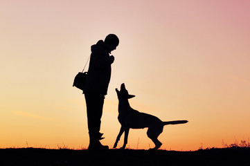 Silhouettes of man and dog on sunset background