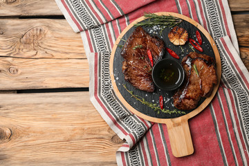 Board with tasty cooked meat, oil and spices on wooden table