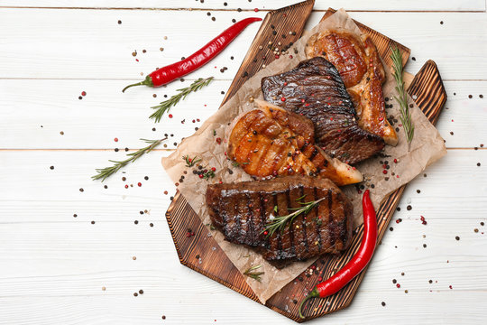 Wooden Board With Different Tasty Cooked Meat And Spices On White Table