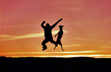 Silhouettes of man and dog on sunset background