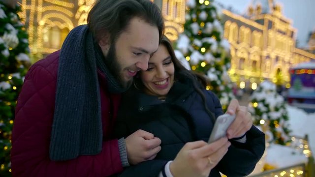 cheerful pair of boyfriend and girlfriend are having fun, watching pictures on display of smartphone