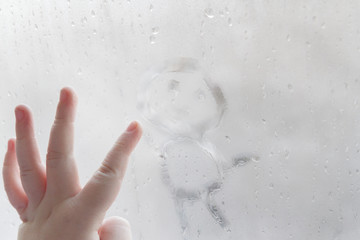 The child's hand draws a man on a frozen misted window in winter