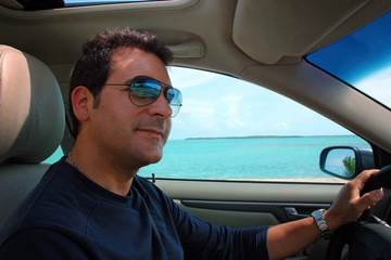Man drives the car, and in the background the blue sea of the ocean.