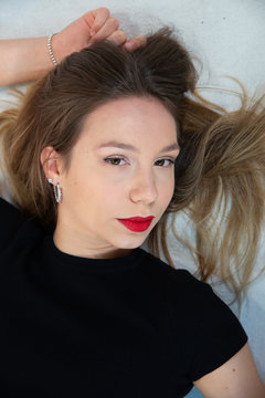 Close-up portrait of the face of a beautiful young blonde woman lying on the floor in a black dress. Girl posing in studio with unkempt hair, image on white background. Perfect makeup with red lips.