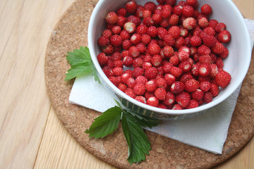 Fresh wild strawberries in a bowl on wooden table