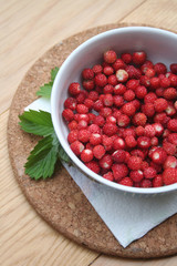 Fresh wild strawberries in a bowl on wooden table