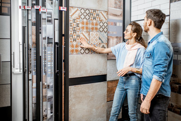 Beautiful young couple choosing ceramic tiles for their house repairment in the building shop