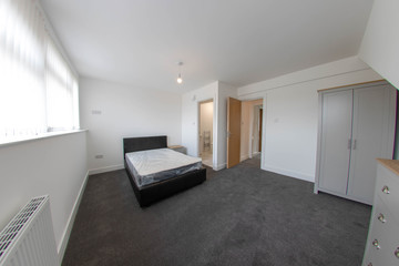 Modern brand new British bedroom, showing a bed and entrance to the ensuite bathroom, the room has white walls with a brown bed with a white mattress.