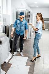 Young woman customer choosing tiles standing with seller or repairman in the ceramic shop