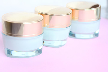 Row of round shiny jars with face cream and selective focus on pink neutral background. Organic natural product for face care. Cosmetic beauty creams in plastic container for skin health. 