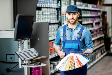 Portrait of a handsome workman with color swatches near the equipment for coloring in the building shop