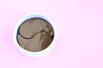 Round white container with black golden anti aging collagen lifting patches under eyes for woman face care with selective focus on pink neutral background. Hydrating beauty facial anti wrinkles patch
