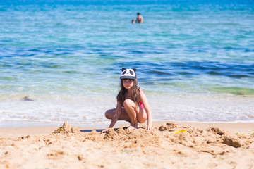 little girl in a red swimsuit on the beach building a sand castle