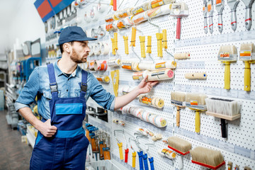 Handsome workman in uniform choosing tools for painting in the building shop