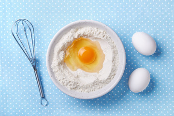 Broken egg yolk and flour in a bowl, whisk and white eggs on the side. Food preparation concept. Baking ingredients. Top view