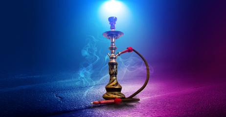 Smoking hookah on the background of an empty room. Multicolored neon light. Searchlight, laser blue and pink rays, smoke.