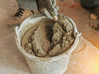 hand hold a trowel and bucket with cement mixed in construction site