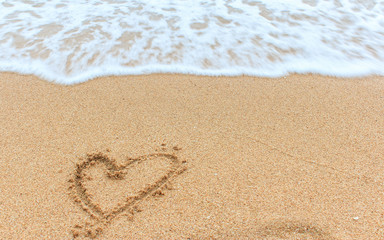 A heart symbol written on a sandy beach with foam and water background. Valentines day concept. 